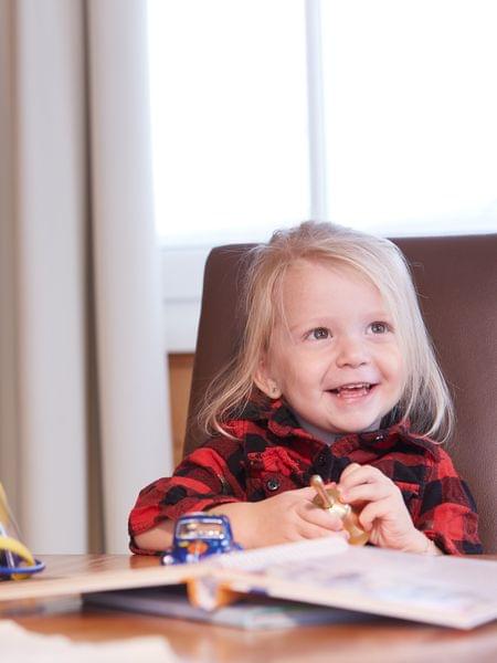 Kleingedrucktes Lächelndes kleines Mädchen am Tisch mit Spielzeug und Kinderbuch